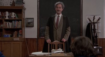 Movie still from “The Meaning of Life” (1983), directed by Terry Jones – An old man in a suit stands at a desk; Medium shot, Over the shoulder angle