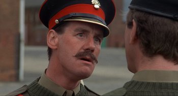 Movie still from “The Meaning of Life” (1983), directed by Terry Jones – A person wearing a uniform; Close Up shot, Over the shoulder angle