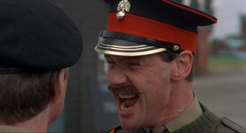 Movie still from “The Meaning of Life” (1983), directed by Terry Jones – A man in a military uniform is laughing at another man; Close Up shot, Low angle