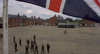 Movie still from “The Meaning of Life” (1983), directed by Terry Jones – A group of men in uniform walking across a dirt field; Extreme Wide shot, High angle