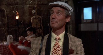 Movie still from “The Meaning of Life” (1983), directed by Terry Jones – A man wearing a hat and a tie; Close Up shot, Over the shoulder angle