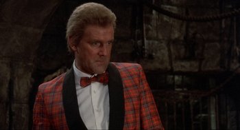 Movie still from “The Meaning of Life” (1983), directed by Terry Jones – A man in a red and black plaid jacket and a bow tie; Close Up shot, Low angle