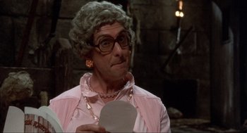 Movie still from “The Meaning of Life” (1983), directed by Terry Jones – An older woman in a pink shirt holding a piece of paper; Close Up shot, Over the shoulder angle