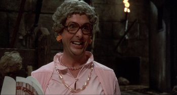 Movie still from “The Meaning of Life” (1983), directed by Terry Jones – An older woman wearing glasses and a pink shirt; Close Up shot, Over the shoulder angle