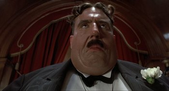 Movie still from “The Meaning of Life” (1983), directed by Terry Jones – A person wearing a suit and bow tie; Close Up shot, Low angle