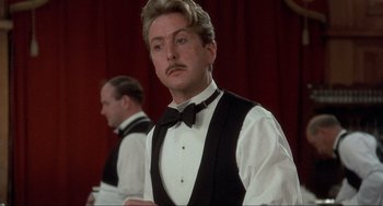 Movie still from “The Meaning of Life” (1983), directed by Terry Jones – A man with a mustache wearing a vest and a bow tie; Close Up shot, Over the shoulder angle
