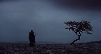 Movie still from “The Meaning of Life” (1983), directed by Terry Jones – A person in a hooded cloak standing on a rocky hill; Extreme Wide shot, Low angle