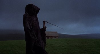 Movie still from “The Meaning of Life” (1983), directed by Terry Jones – A person in a hooded cloak holding a stick in a grassy field; Wide shot, Low angle