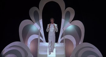 Movie still from “The Meaning of Life” (1983), directed by Terry Jones – A man walking down a flight of stairs in front of an art deco design; Wide shot, Low angle