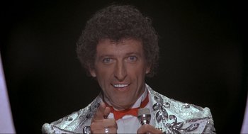 Movie still from “The Meaning of Life” (1983), directed by Terry Jones – A person wearing a suit and tie; Close Up shot, Low angle