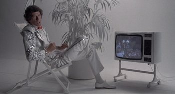 Movie still from “The Meaning of Life” (1983), directed by Terry Jones – A man sitting in a chair in front of a television; Wide shot, Low angle