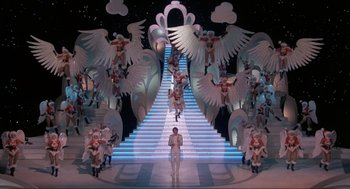 Movie still from “The Meaning of Life” (1983), directed by Terry Jones – A man standing in front of a staircase surrounded by angels; Extreme Wide shot, High angle