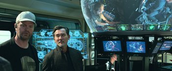 Movie still from “The Meg” (2018), directed by Jon Turteltaub – A man standing in front of a tv screen; Medium shot, Over the shoulder angle