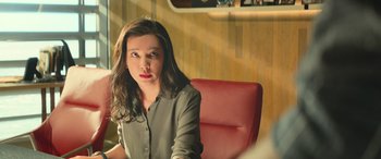 Movie still from “The Meg” (2018), directed by Jon Turteltaub – A woman sitting on a red chair in a room; Close Up shot, Over the shoulder angle