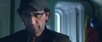 Movie still from “The Meg” (2018), directed by Jon Turteltaub – A person wearing glasses and a hat; Close Up shot, Over the shoulder angle
