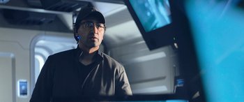 Movie still from “The Meg” (2018), directed by Jon Turteltaub – A man wearing glasses and a hat is standing in front of a monitor; Close Up shot, Low angle