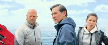 Movie still from “The Meg” (2018), directed by Jon Turteltaub – Two men standing next to each other near the ocean; Medium shot, Low angle