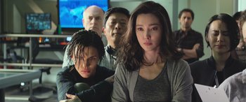 Movie still from “The Meg” (2018), directed by Jon Turteltaub – A group of people standing next to each other in front of a tv; Medium shot, High angle