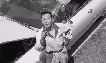 Movie still from “The Misfits” (1961), directed by John Huston – An old photo of a man holding a baseball bat in front of an airplane; Medium shot, Low angle