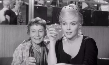 Movie still from “The Misfits” (1961), directed by John Huston – A woman and a woman holding a glass of wine; Medium shot, Over the shoulder angle
