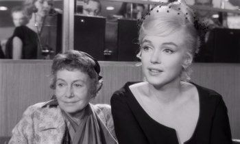 Movie still from “The Misfits” (1961), directed by John Huston – A woman sitting next to another woman in a black and white photo; Medium shot, Over the shoulder angle