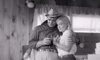 Movie still from “The Misfits” (1961), directed by John Huston – A man and a woman are hugging and holding a drink; Medium shot, Low angle