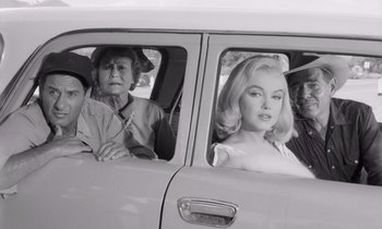Movie still from “The Misfits” (1961), directed by John Huston – A group of people sitting in the back of a car; Medium shot, High angle