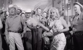 Movie still from “The Misfits” (1961), directed by John Huston – An old photo of a woman in a cowboy hat dancing; Medium shot, Low angle