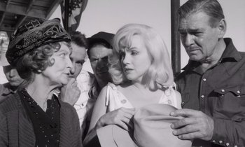 Movie still from “The Misfits” (1961), directed by John Huston – A group of people standing around a woman; Medium shot, Over the shoulder angle