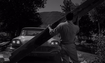 Movie still from “The Misfits” (1961), directed by John Huston – A black and white photo of a man holding a large piece of wood; Wide shot, Low angle