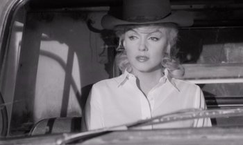 Movie still from “The Misfits” (1961), directed by John Huston – A black and white photo of a woman wearing a cowboy hat; Medium shot, Over the shoulder angle