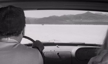 Movie still from “The Misfits” (1961), directed by John Huston – A man driving a car on a road; Wide shot, High angle