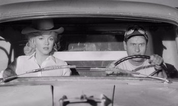 Movie still from “The Misfits” (1961), directed by John Huston – A man and a woman sitting in the drivers seat of a car; Medium shot, Low angle