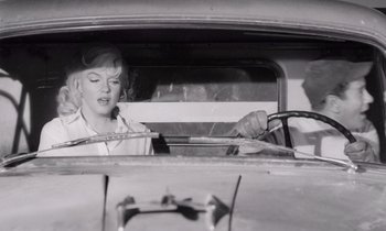 Movie still from “The Misfits” (1961), directed by John Huston – An old black and white photo of a woman driving a car; Medium shot, Over the shoulder angle