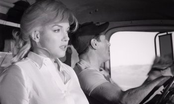 Movie still from “The Misfits” (1961), directed by John Huston – A man and a woman driving a car in the road; Medium shot, Low angle