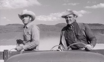 Movie still from “The Misfits” (1961), directed by John Huston – Two men in cowboy hats sitting in the drivers seat of an old car; Medium shot, Low angle
