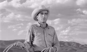Movie still from “The Misfits” (1961), directed by John Huston – A man wearing a cowboy hat and holding a whip; Medium shot, Low angle