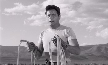 Movie still from “The Misfits” (1961), directed by John Huston – A black and white photo of a man holding ropes; Medium shot, Low angle