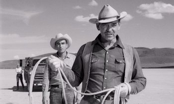 Movie still from “The Misfits” (1961), directed by John Huston – A man in a cowboy hat holding a lasso while standing next to another man; Medium shot, Low angle