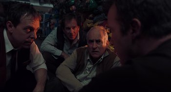 Movie still from “The Mist” (2007), directed by Frank Darabont – A group of men sitting next to each other on a couch; Medium shot, Over the shoulder angle