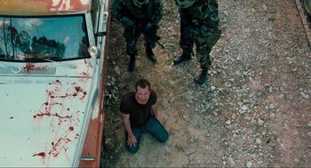 Movie still from “The Mist” (2007), directed by Frank Darabont – A man is sitting on the ground in front of a group of soldiers; Wide shot, High angle