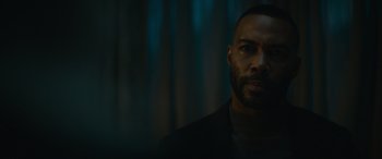 Movie still from “The Mother” (2023), directed by Niki Caro – A man with a beard is standing in a dark room; Close Up shot, Over the shoulder angle