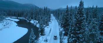 Movie still from “The Mother” (2023), directed by Niki Caro – A car driving down a snow covered forest road; Extreme Wide shot, High angle