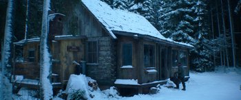 Movie still from “The Mother” (2023), directed by Niki Caro – An old log cabin in the snow near a forest; Wide shot, High angle