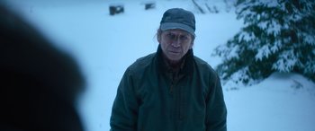 Movie still from “The Mother” (2023), directed by Niki Caro – A man wearing a hat and a green jacket in the snow; Close Up shot, Over the shoulder angle