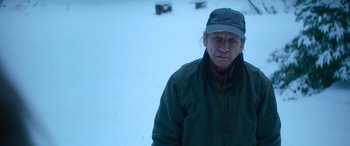 Movie still from “The Mother” (2023), directed by Niki Caro – A man wearing a hat and a green jacket in the snow; Close Up shot, Over the shoulder angle