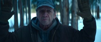 Movie still from “The Mother” (2023), directed by Niki Caro – An older man wearing a hat and a jacket; Close Up shot, Low angle