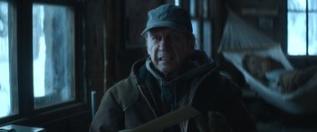 Movie still from “The Mother” (2023), directed by Niki Caro – An older man wearing a hat and a jacket; Close Up shot, Over the shoulder angle