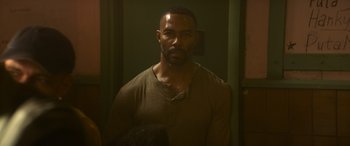 Movie still from “The Mother” (2023), directed by Niki Caro – A man in a brown shirt is standing in a room; Close Up shot, Over the shoulder angle