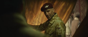 Movie still from “The Mother” (2023), directed by Niki Caro – A man in a military uniform wearing a maroon hat; Medium shot, Low angle